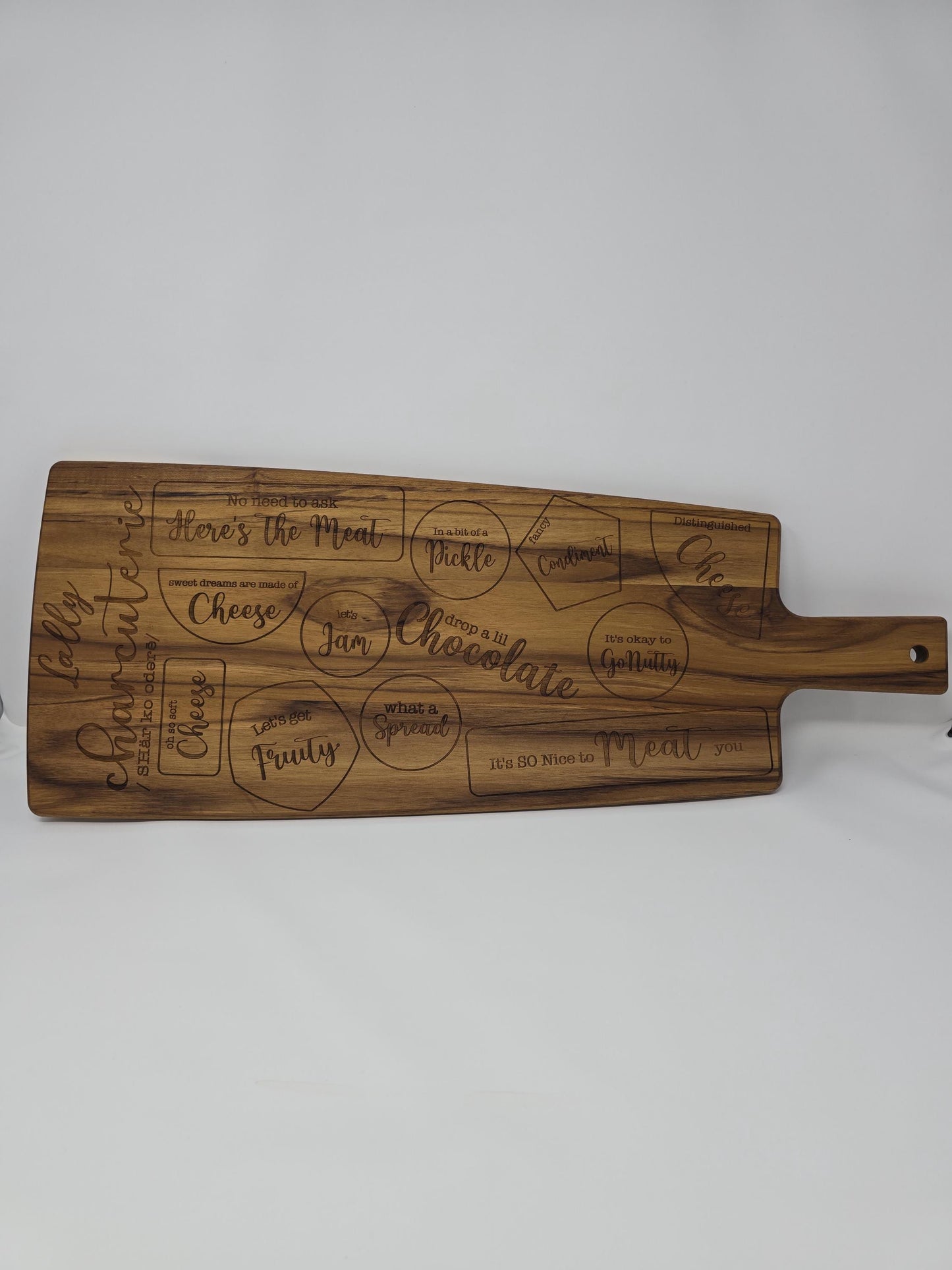Personalized engraved wooden cutting board with a name and the word "charcuterie" engraved on it, featuring designated spots for meats, cheeses, crackers, and other charcuterie items