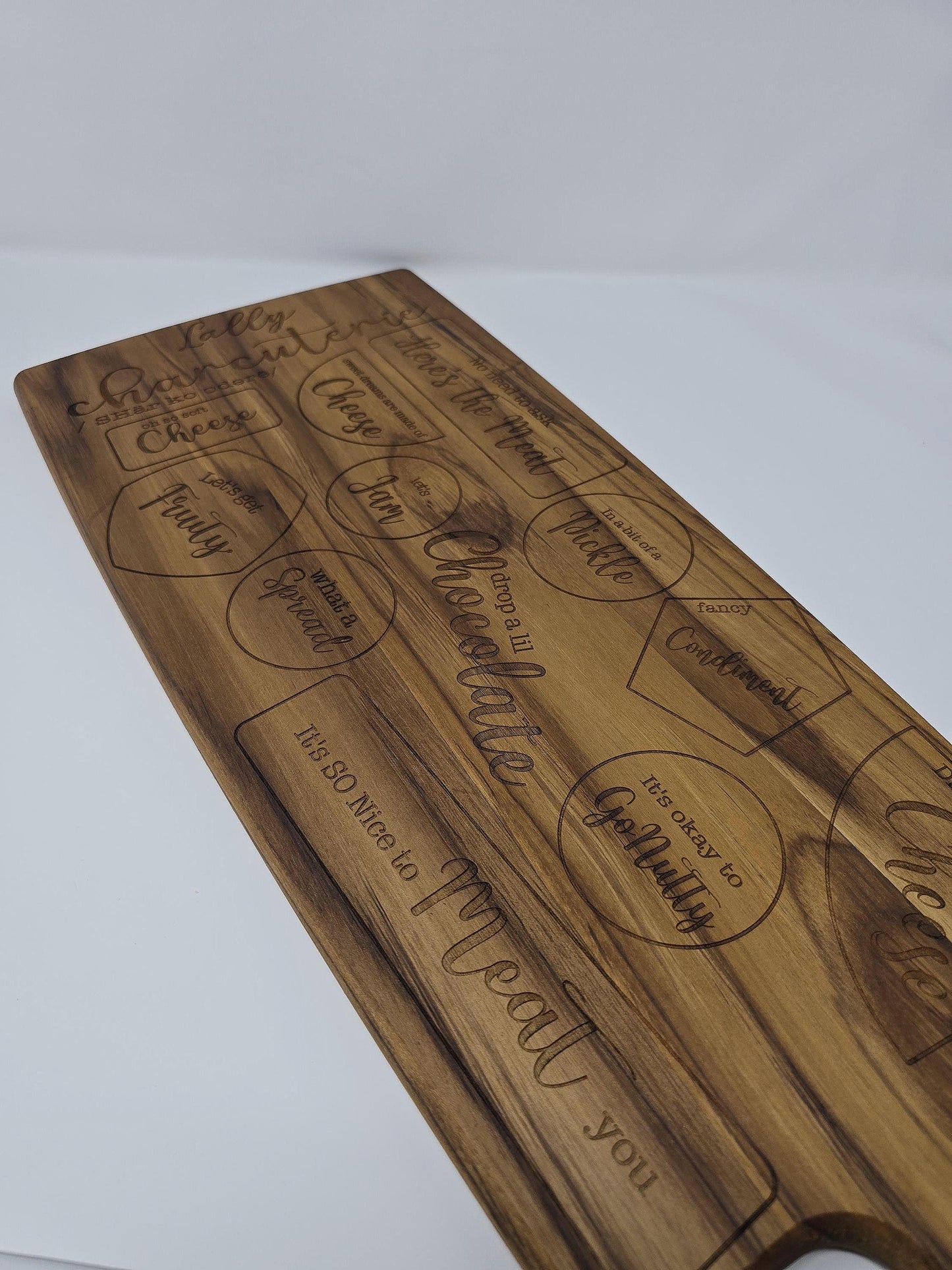 Personalized engraved wooden cutting board with a name and the word "charcuterie" engraved on it, featuring designated spots for meats, cheeses, crackers, and other charcuterie items