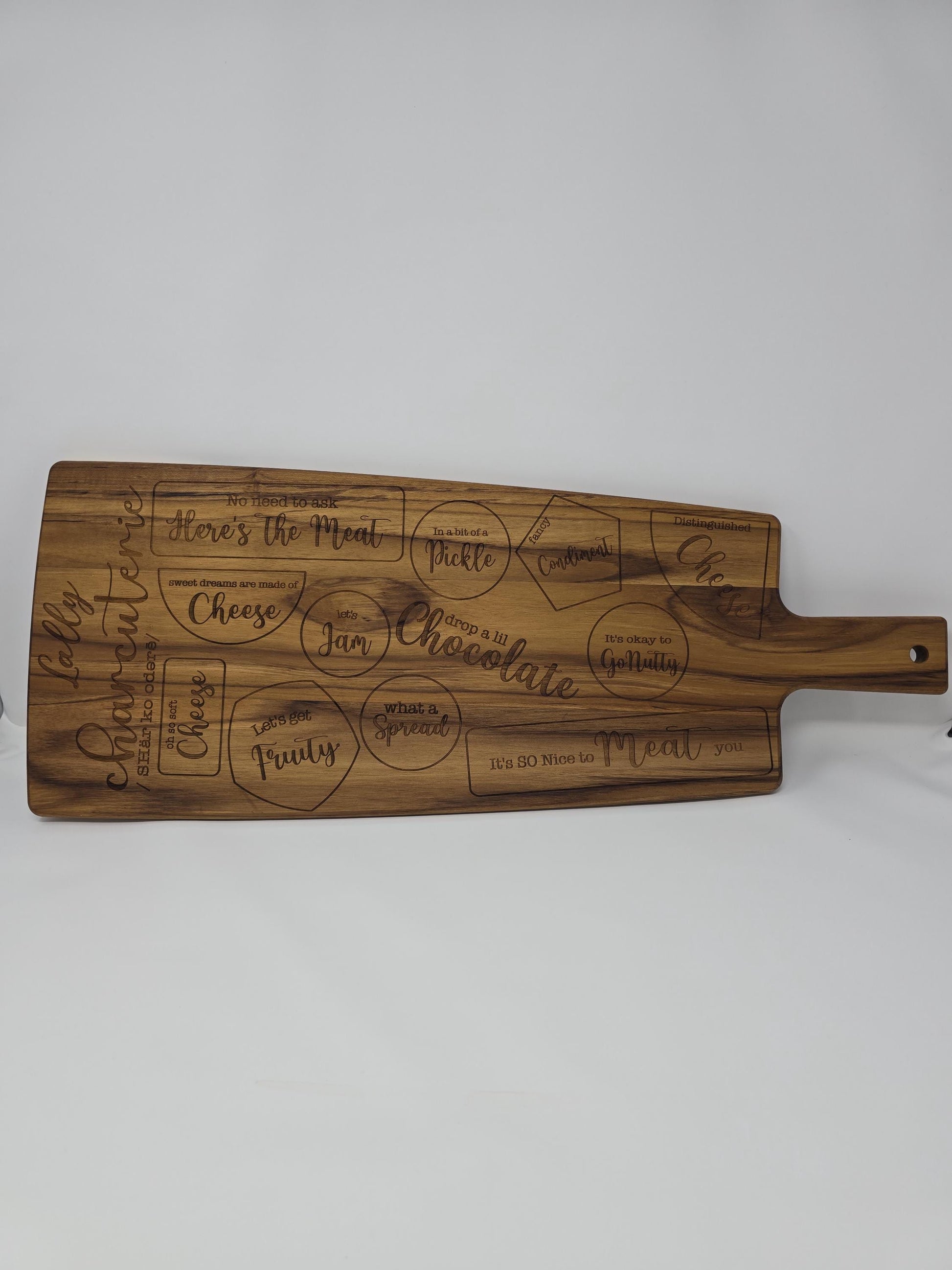 Personalized engraved wooden cutting board with a name and the word &quot;charcuterie&quot; engraved on it, featuring designated spots for meats, cheeses, crackers, and other charcuterie items